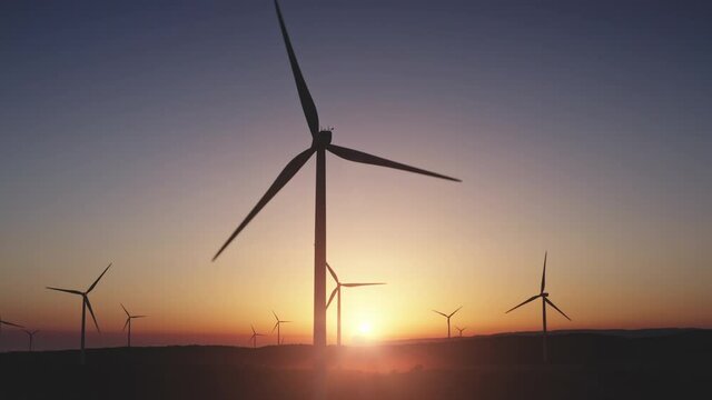 Wind turbines silhouette blades rotate in colorful sunset Aerial view slow motion drone flight. Wind mill farm in evening field. Alternative green energy production. Generation electricity. Yellow sun