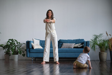 Happy mindful single mother doing morning exercises in yoga pose with kid playing at home. morning...
