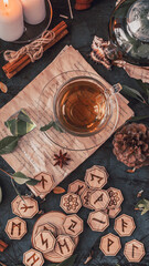 Wooden runes are lying on the table among the papers with notes. There is a mug of tea next to it. Astrology and esotericism. Esoteric breakfast.