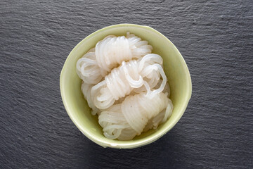 器に盛られたしらたき・コンニャクから作った麺状の食材（石製スレートプレート・黒背景）