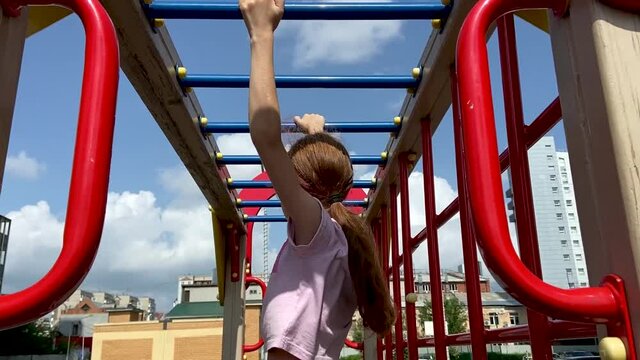 Girl with long hair grabs with her hands and moves along the handle ladder. Construction on the playground 