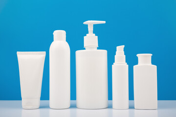 Set of white unbranded cosmetic bottles for daily skincare against bright blue background. Concept of hygiene and man's skin care 