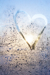 unfocus symbol of beautiful heart with the sun inside painted on misted glass, moonlight, texture of frost and water drops, empty space for an inscription. vertical frame out of focus