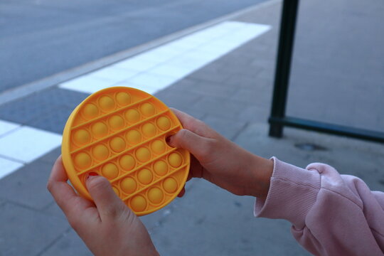 Female hands playing with a yellow fidget toy. Pink arm or shirt holding the plastic device. Close up and isolated. Copy space for text. Stockholm, Sweden, Europe.