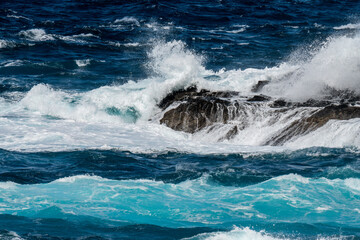 Naklejka premium Atlantik ocean rollers breaking on black lava rocks at the north coast of Madeira in front of the promenade of Porto Moniz
