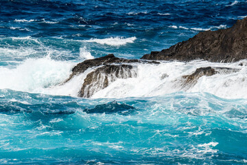 Atlantik ocean rollers breaking on black lava rocks at the north coast of Madeira in front of the promenade of Porto Moniz