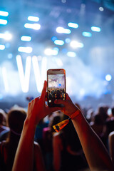 Fototapeta na wymiar Using a smartphone in a public event, live music festival. Holding a mobile phone in hands and shooting photo or video content. Youth, party, vacation concept.