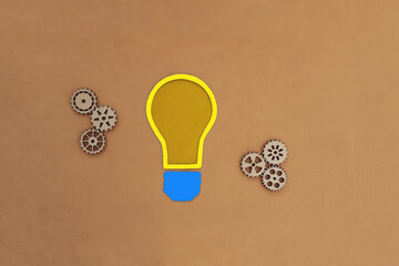 Electric light bulb, wooden gears on a beige background. The mechanism of creativity, solutions, ideas.