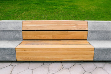 Street modern park bench. A bench made of wood and concrete against the backdrop of a lawn. Urban interior. A place to relax outside.