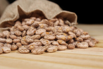 Burlap Bag of Dried Pinto Beans Spilled on Wooden Table