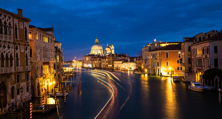 Fototapeta na wymiar Beautiful view in the night at Cityscape image of Grand Canal in Venice, with Santa Maria della Salute Basilica reflected in calm sea. Lights of passenger boat on the water.