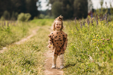 A little girl in a brown dress, laughing, runs across the field