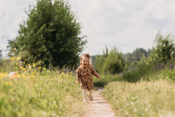 A little girl in a brown dress, laughing, runs across the field