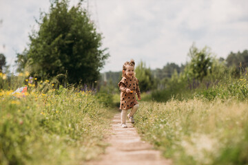 A little girl in a brown dress, laughing, runs across the field