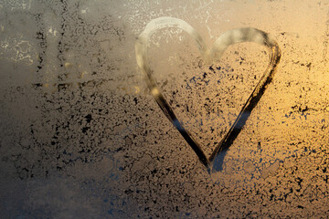 symbol of beautiful heart with the yellow sunlight painted on misted glass, texture of frost and water drops, empty space for an inscription. frame out of focus, copy space for an inscription