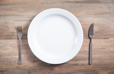Empty plate with fork and knife on wooden table.