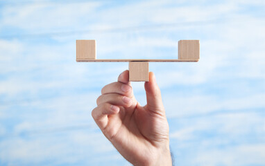 Male hand holding balance scales made in from wooden cubes.