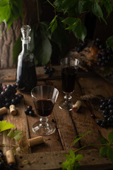 Red wine scene with decanter,crystal glasses,fresh grapes and green twigs on vintage wooden...