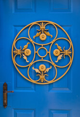 Traditional and decorative ornament made of iron placed on a blue wooden door. Beautiful iron craftwork painted gold.