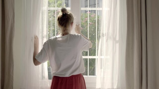 Woman opening window to get some fresh air on a sunny warm day, 4k, 50 fps footage.