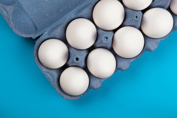 Brown chiken eggs in a paper tray on a blue surface, flat view