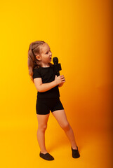 girl singer on a yellow background with a microphone in her hands is learning to sing. Vocal lesson at school