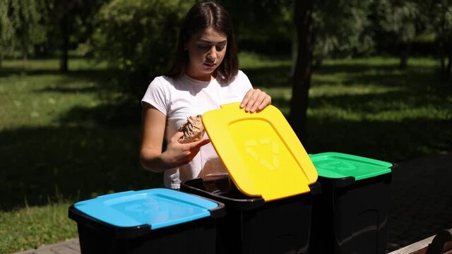 Middle selection of female hold two different type of rubbish, plastic container and paper and thowing into different recycling bins. Close-up of woman stand by blue, yeallow and green bin