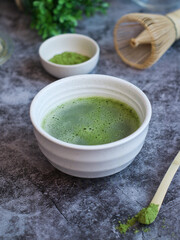 A bowl of traditional Japanese matcha green tea with its powder and chesen whisk in background on a wooden table. A healthy antioxidant food and drink concept 