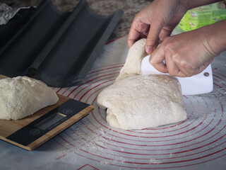 Hands cutting an uncooked traditional French baguette dough to divide a bread on preparation for...