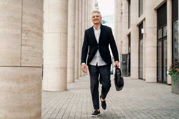 A successful entrepreneur goes to work in the morning. A freelancer in a business suit. A man of European appearance fashionable hairstyle gray hair. He holds a bag with documents in his hand.