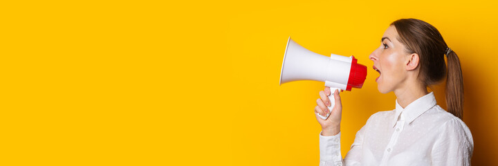 Young woman in a white shirt shouts into a megaphone on a yellow background. Concept for hiring,...
