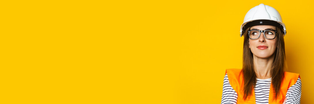 Young woman with a pensive face in a vest and hard hat on a yellow background. Construction concept, new building. Banner