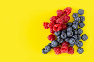 Delicious fresh organic blueberries and raspberries on bright yellow background with copy space.