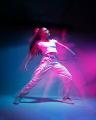 Dancing mixed race young girl in colourful neon studio light. Female dancer in white stylish...