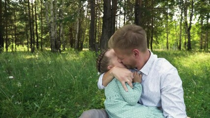A father tenderly holds his daughter in his arms. The little girl hugs and kisses her father tenderly. Dad and his five-year-old daughter
