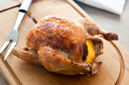 Whole roast chicken with lemon stuffing on wooden board with carving fork