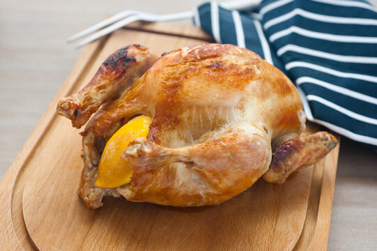 Roast Chicken with lemon on wooden board ready to be carved