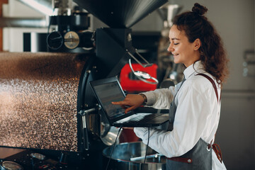 Coffee roaster machine and barista woman with laptop computer at coffee roasting process.