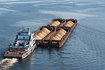 A tugboat pushes barges with sand on calm water, top view