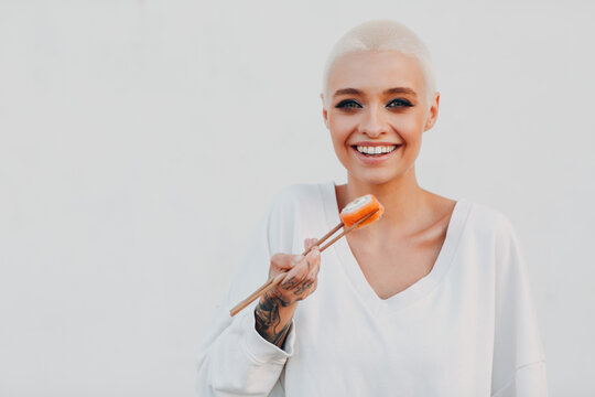 Portrait Of Young Smiling Millenial European Short Haired Woman Eating Sushi Philadelphia Salmon Roll . Beautiful Happy Blonde Girl Outdoor.