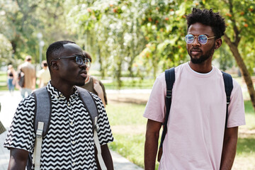 Two African students talking to each other while walking through the park together