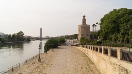 Views of the promenade along the Guadalquivir river, the Torre del Oro, the Triana bridge and the Torre Sevilla skyscraper on a cloudy day in Seville (Andalusia, Spain).