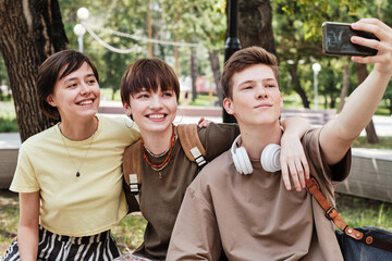 Teenage boy holding his mobile phone and making selfie portrait with his friends during meeting in the park