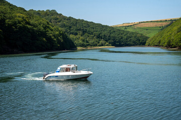 Looe, Cornwall, England, UK. 2021. A small cabin cruiser on the River Looe with a backdrop of Cornish countryside.
