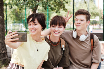 Group of students making selfie portrait together on mobile phone while sitting in the park