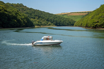 Obraz premium Looe, Cornwall, England, UK. 2021. A small cabin cruiser on the River Looe with a backdrop of Cornish countryside.
