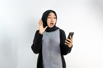 Beautiful young asian Muslim woman surprised, wow expression, got something unexpected, looking at smartphone isolated on white background, advertising concept