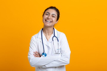 Fototapeta premium Portrait of ilaughing smiling ndian doctor woman in white medical gown stethoscope isolated on yellow background.