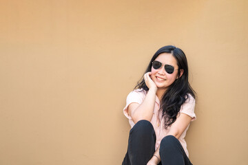 Relaxed Pretty Asian Woman sits on the rooftop floor with a light brown background and smiles to the camera.