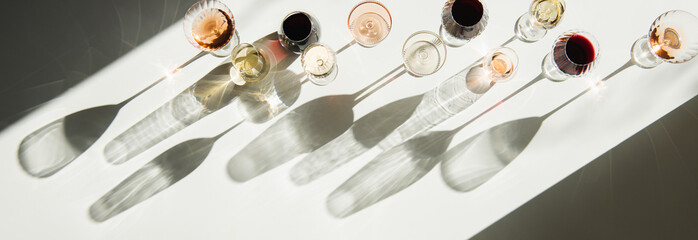 Glasses of wine on white table with shades, top view, copy space